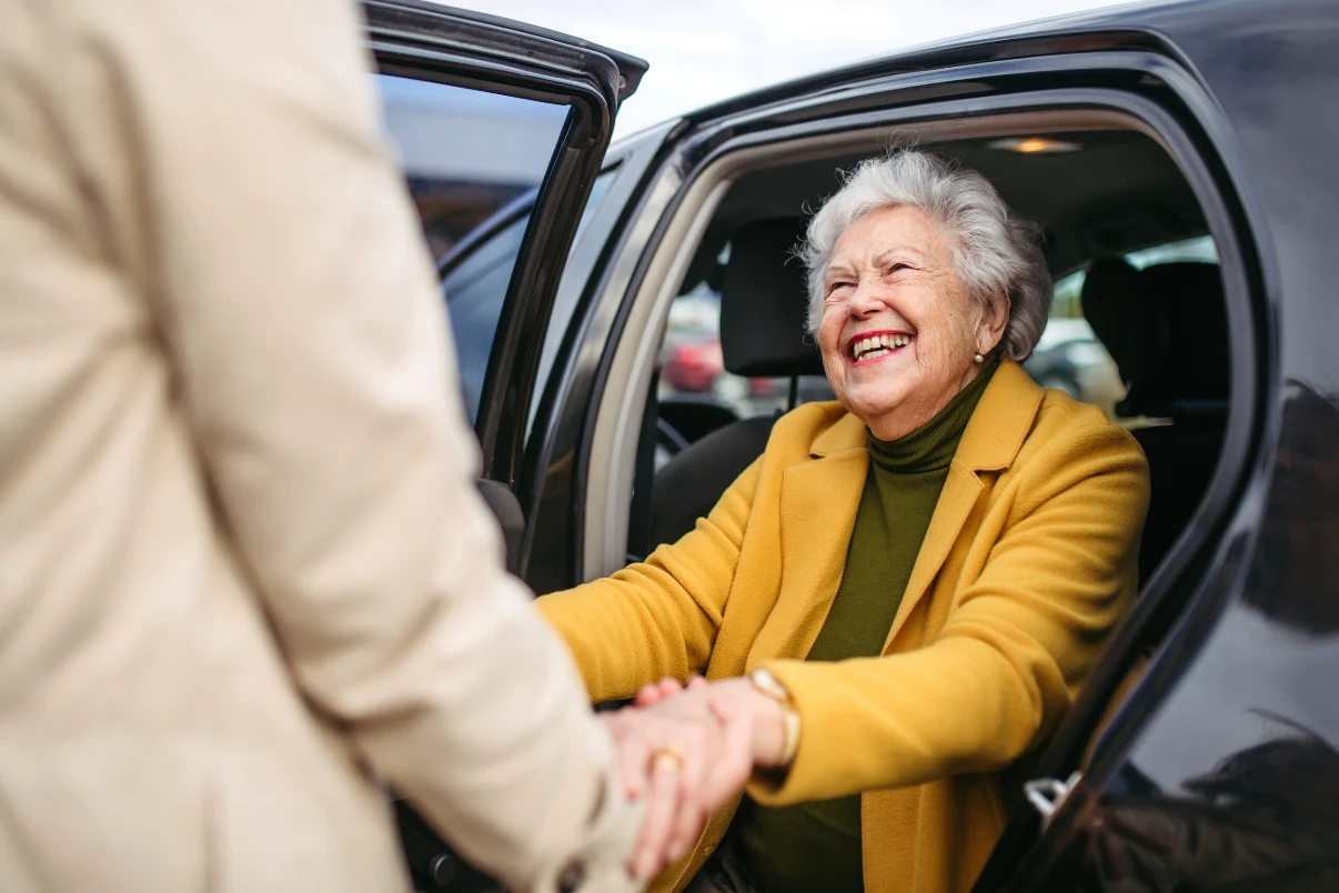 Un chauffeur aide une dame âgée souriante à sortir du véhicule